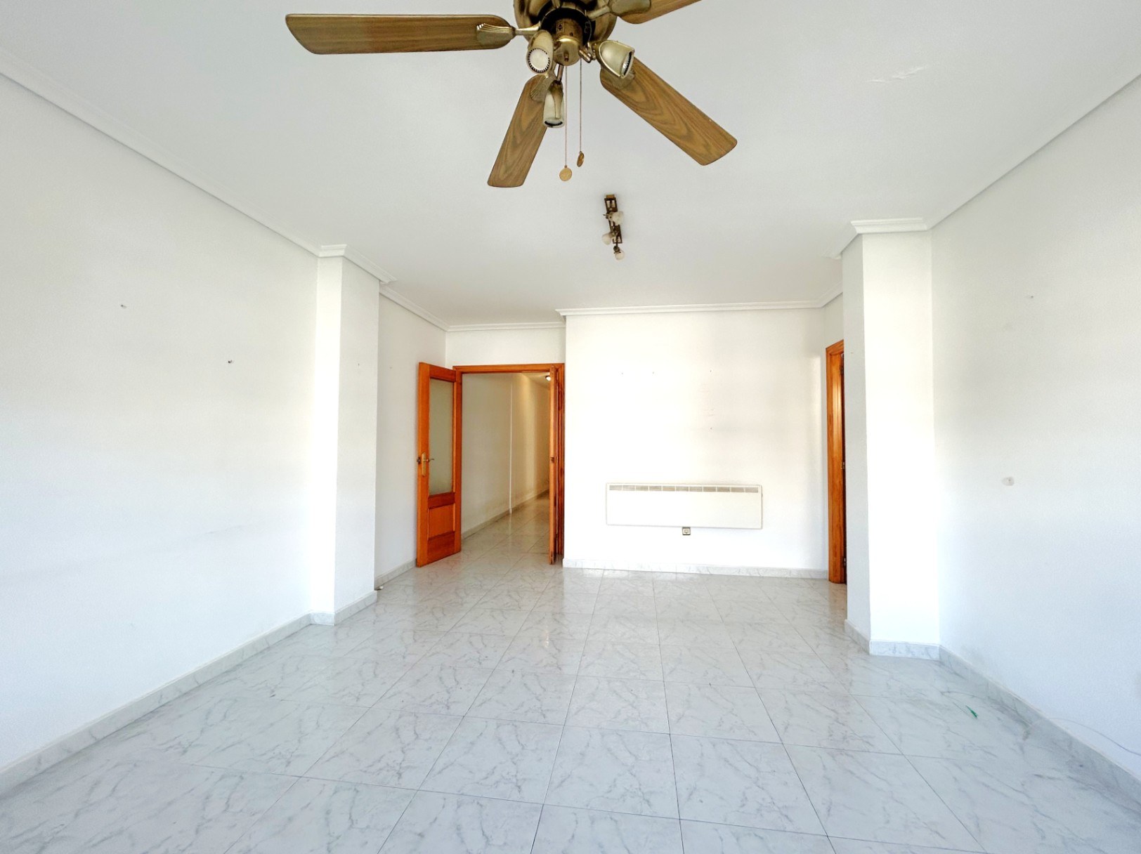 Amplio salón diáfano con suelos de gres efecto mármol, paredes blancas y ventilador de techo de madera. Incluye calefacción de pared y carpintería interior en madera natural.