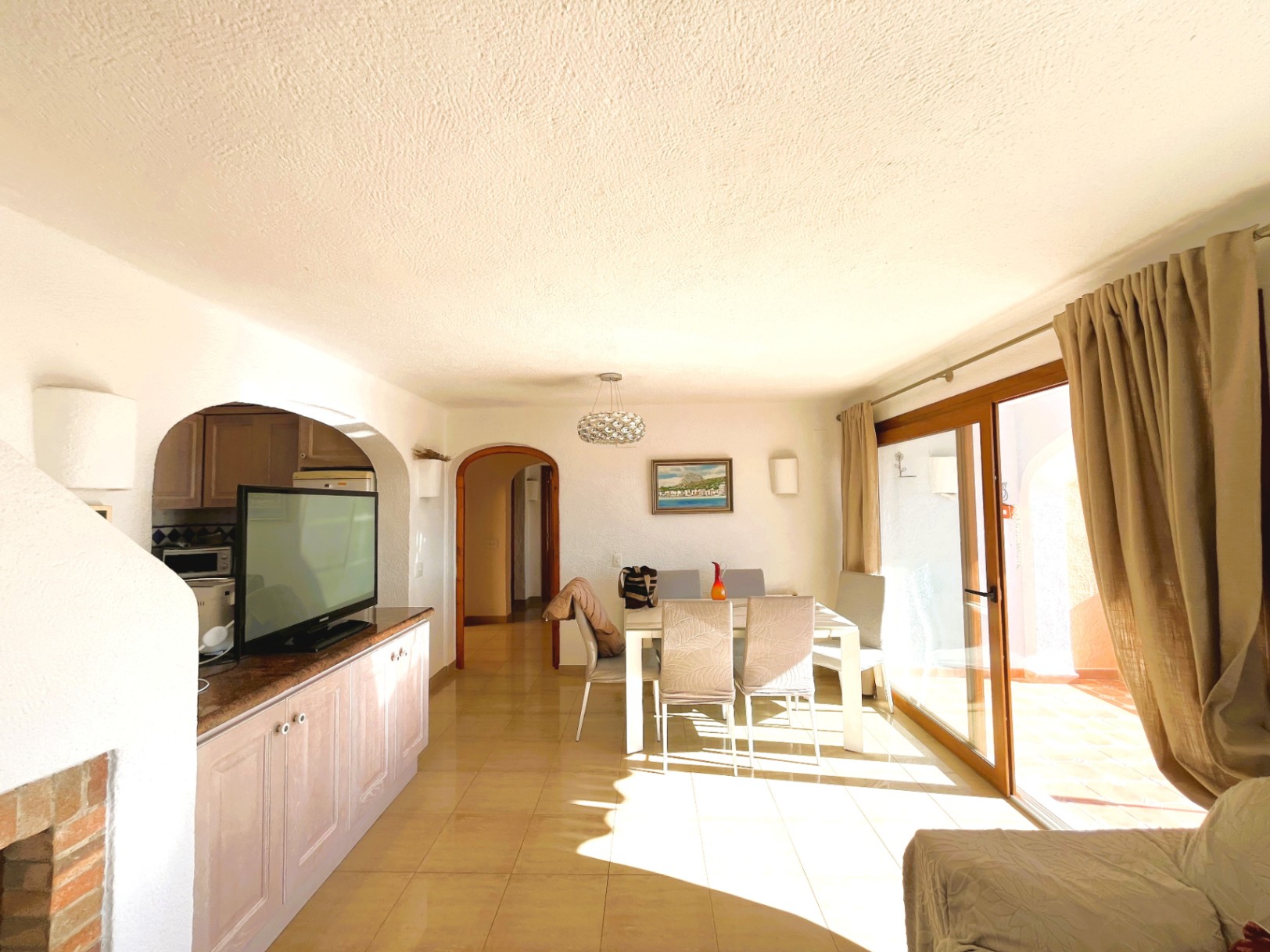 Salón comedor luminoso con suelos cerámicos, acceso directo a la terraza mediante ventanales de madera y una distribución abierta que conecta con la cocina.
