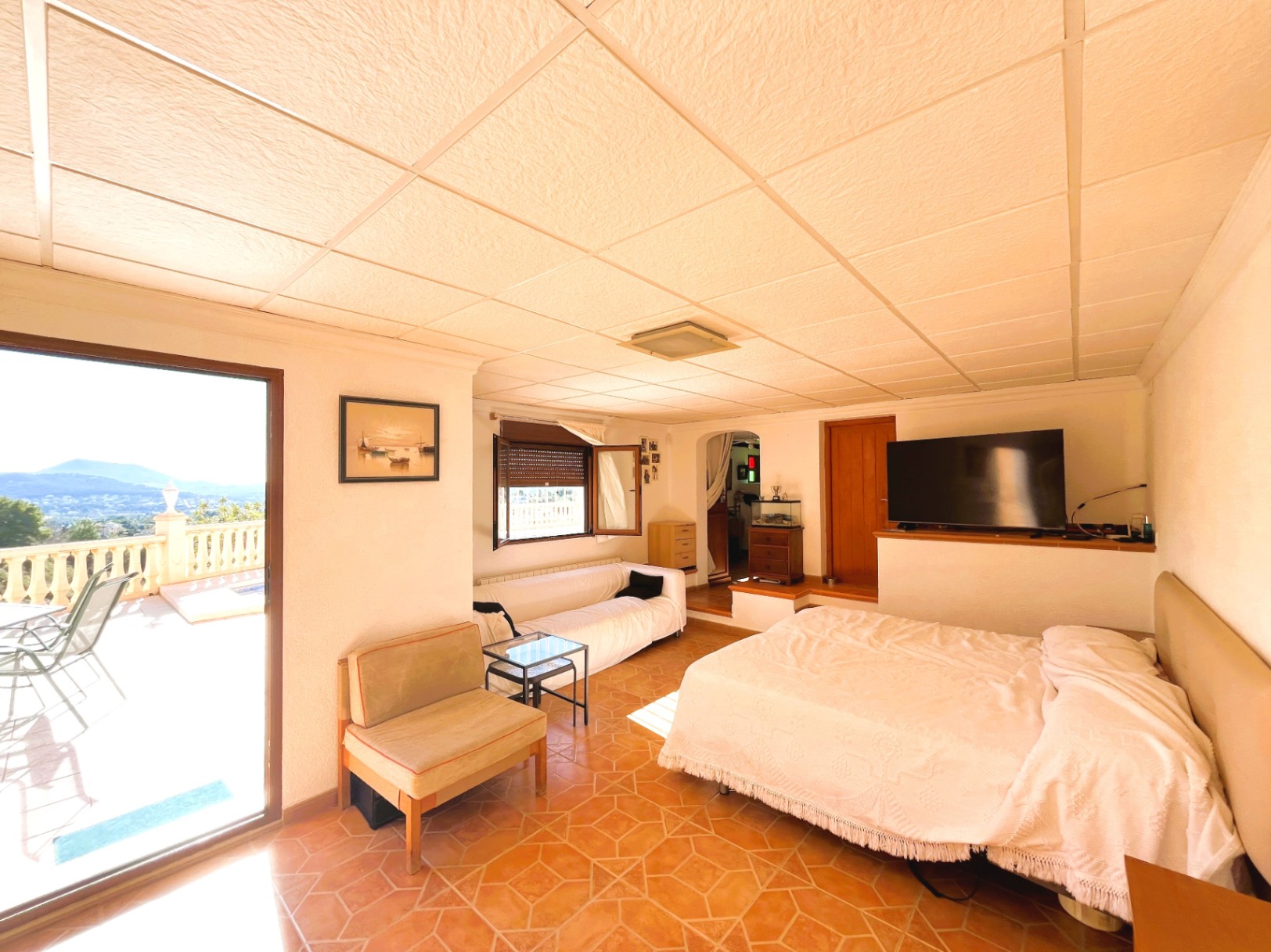 Salón independiente en planta inferior con zona de dormitorio, suelos cerámicos y acceso directo a la terraza con vistas panorámicas.
