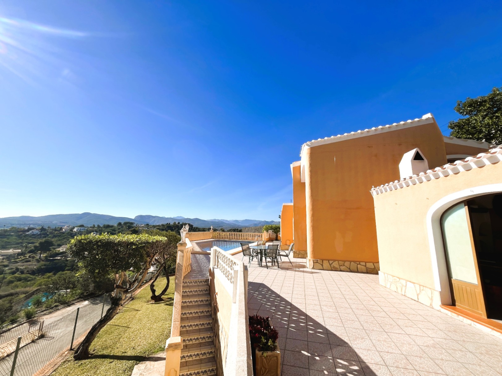 Terraza principal con orientación sur, zona de comedor exterior y vistas panorámicas a las montañas. Incluye acceso a la piscina privada y escaleras laterales.