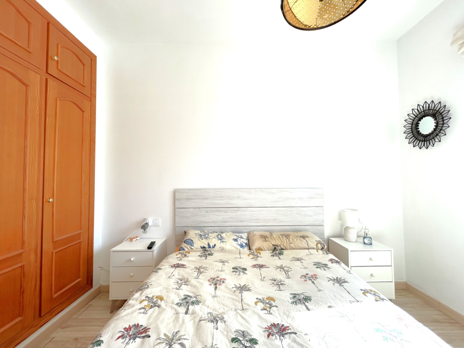 Dormitorio doble con armario empotrado de madera, mesitas de noche blancas y cabecero de madera clara. La estancia cuenta con suelos laminados y abundante luz natural.