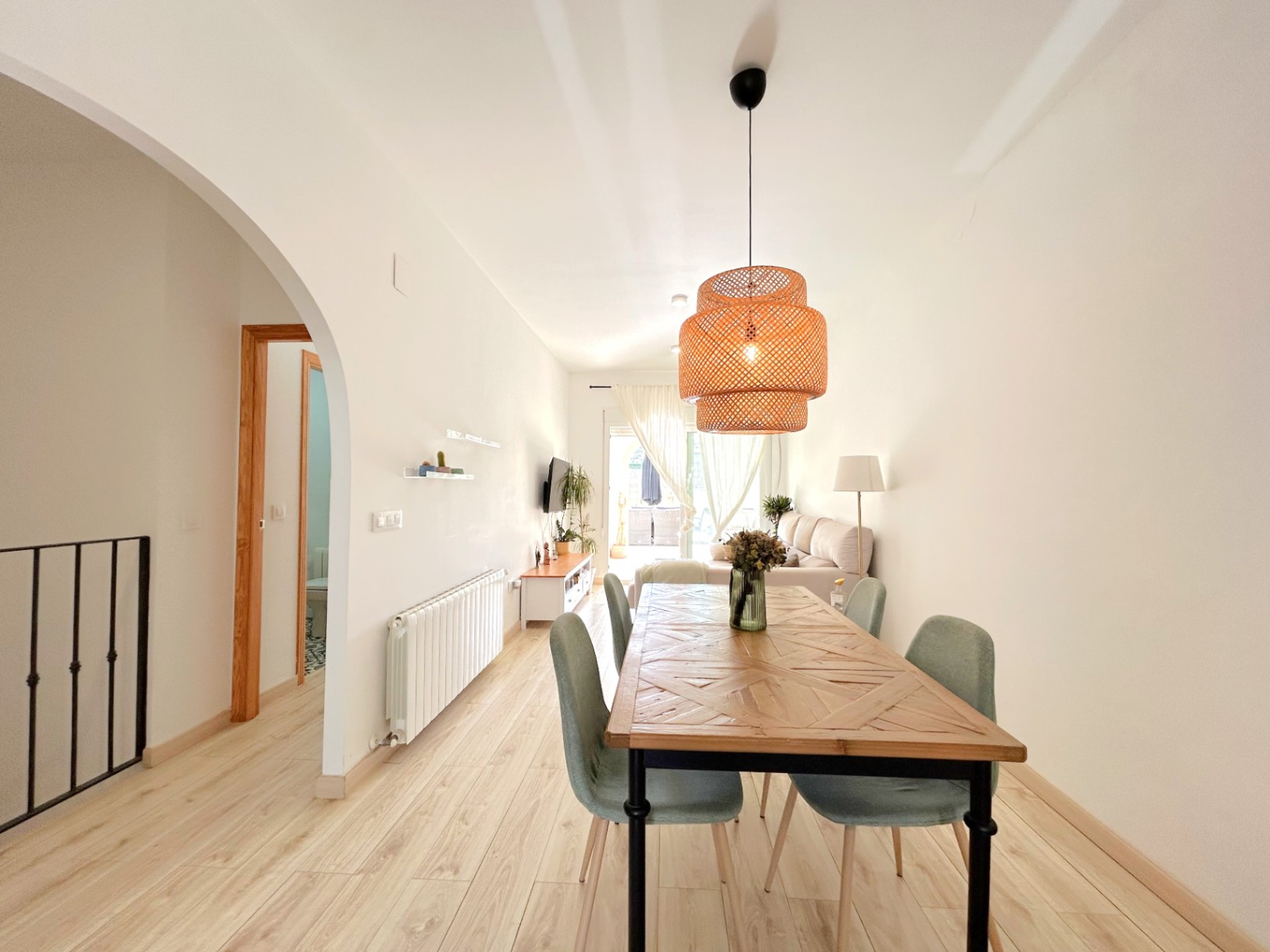 Salón comedor de concepto abierto con suelos de madera clara, mesa con diseño geométrico y lámpara de fibras naturales. Incluye calefacción por radiadores y acceso a la terraza.
