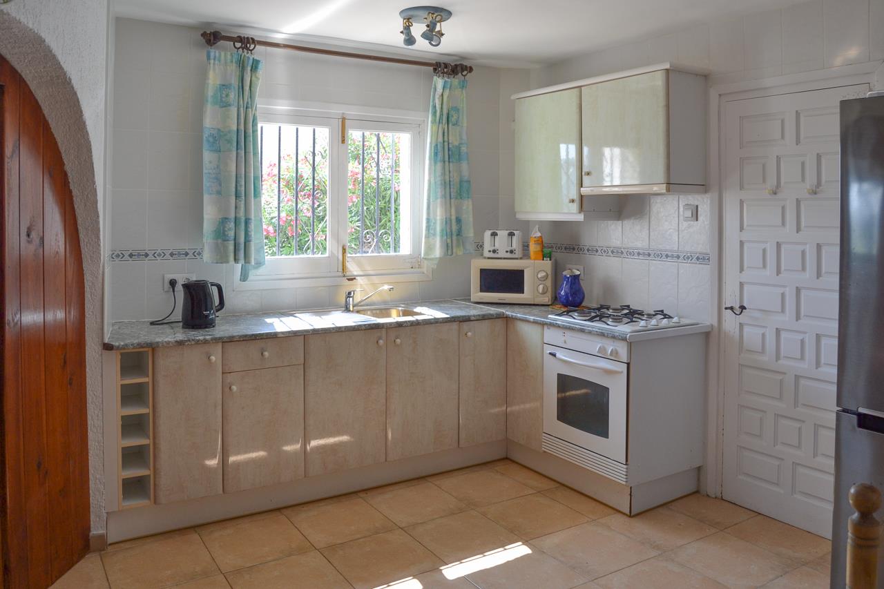 Cocina funcional con armarios en tonos crema, encimera de granito y equipamiento completo con horno blanco y placa de gas, iluminada por luz natural.