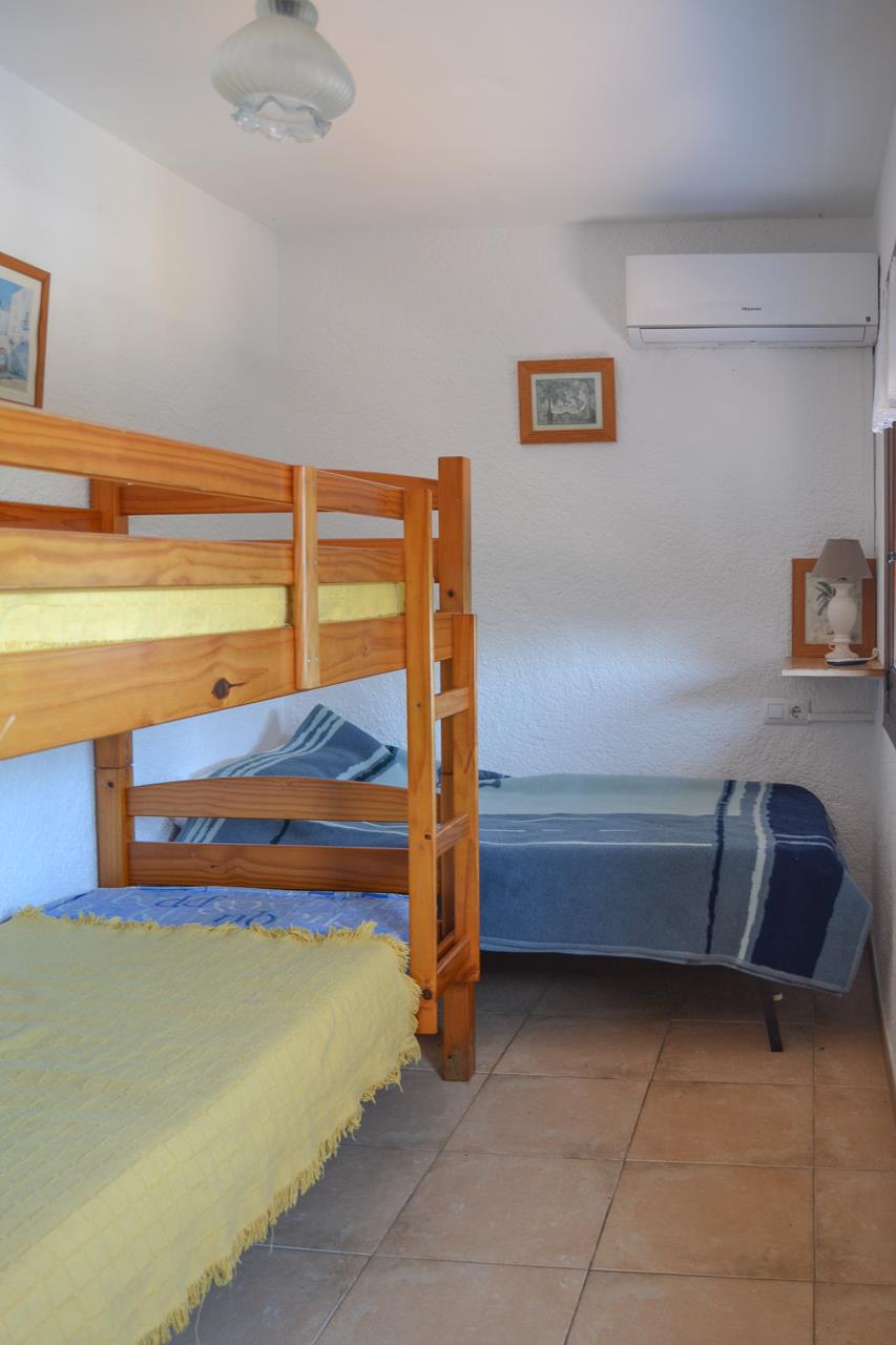 Dormitorio con literas de madera de pino y cama individual, equipado con aire acondicionado, suelos de gres y paredes de acabado rugoso.