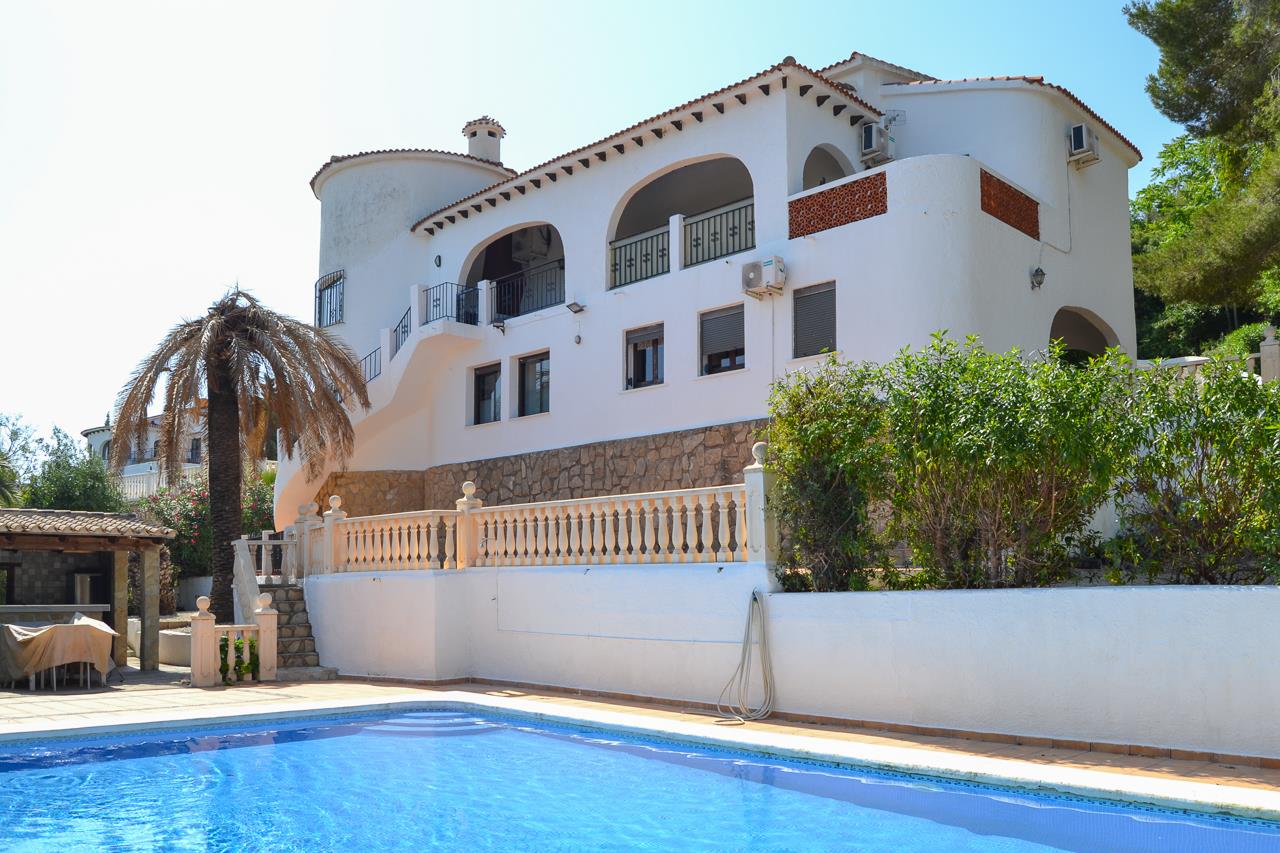 Vista exterior de la villa con piscina de 12x6 metros, terrazas cubiertas con arcos y fachada blanca tradicional sobre zócalo de piedra natural.