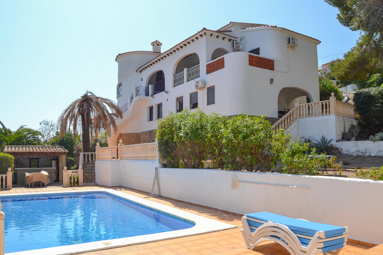 Vista exterior de la villa con piscina privada, amplias terrazas soleadas y arquitectura mediterránea tradicional con arcos y detalles en piedra.