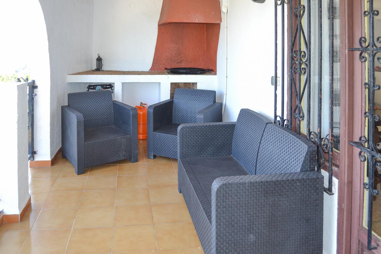 Zona de naya cubierta con mobiliario de ratán sintético oscuro, suelo cerámico y barbacoa de obra integrada con campana en tono arcilla.