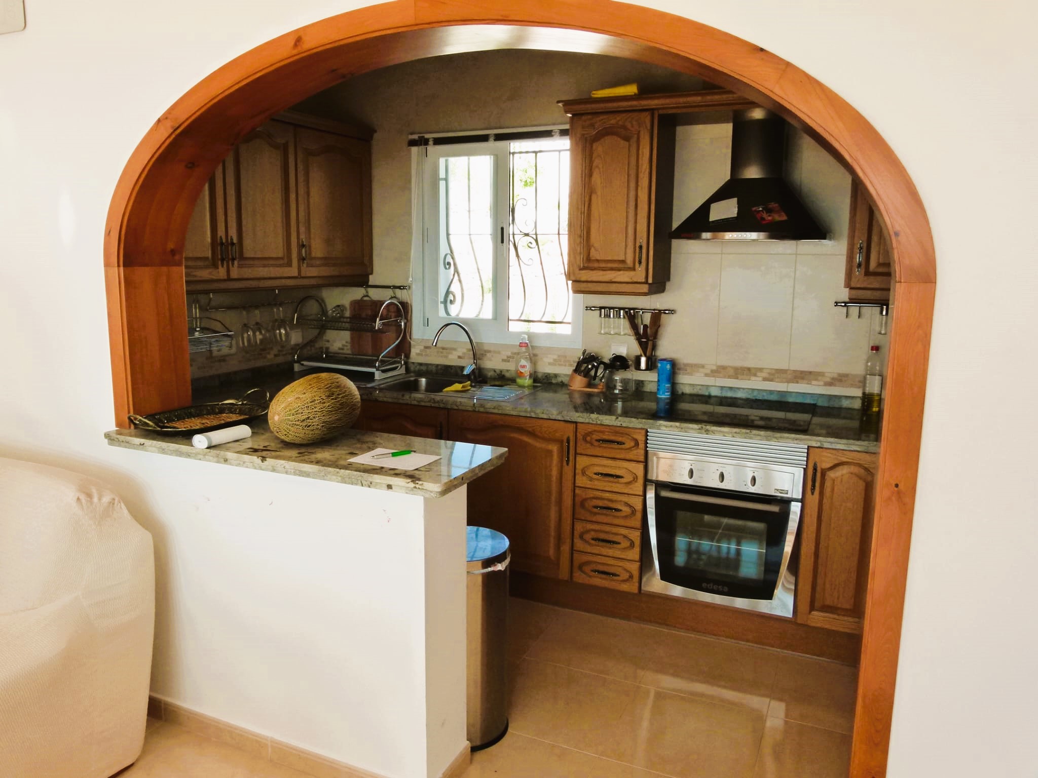 Cocina con arco de madera, muebles color miel y encimera de granito. Estilo rústico y funcional.