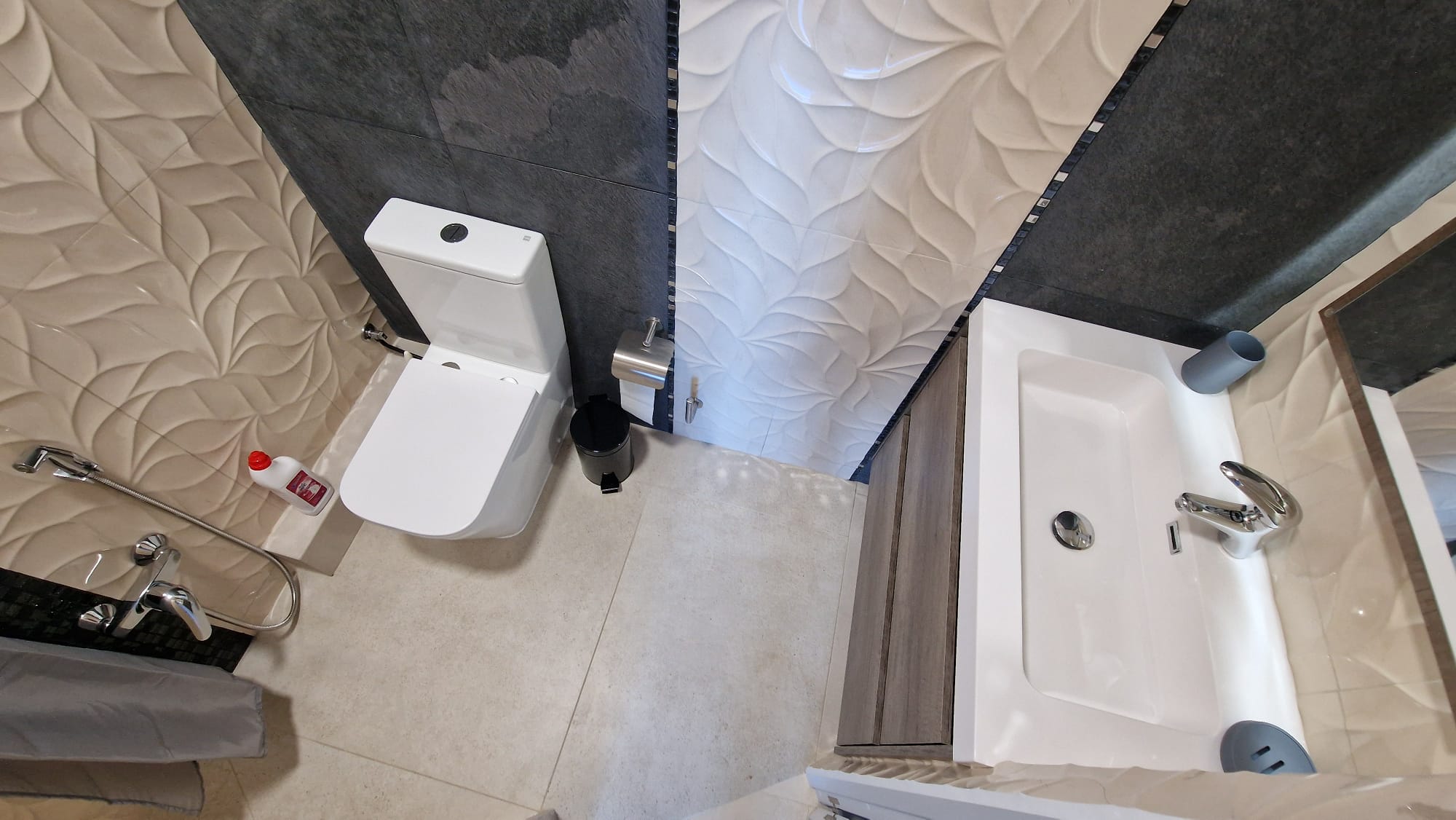 Detalle de baño con azulejos texturizados, inodoro blanco y lavabo moderno. Diseño funcional y elegante.