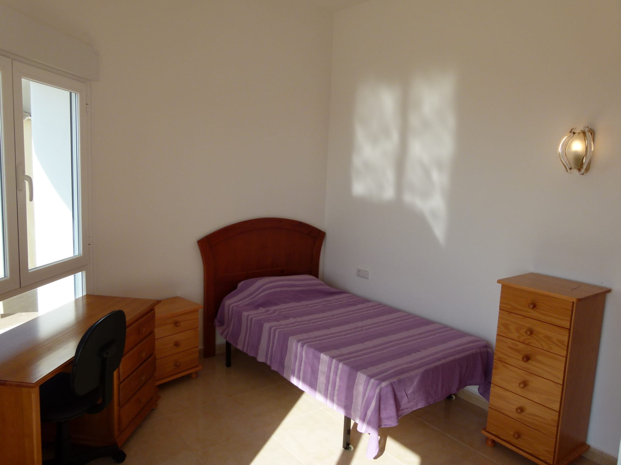 Dormitorio luminoso con cama individual, escritorio de madera y cómoda a juego.