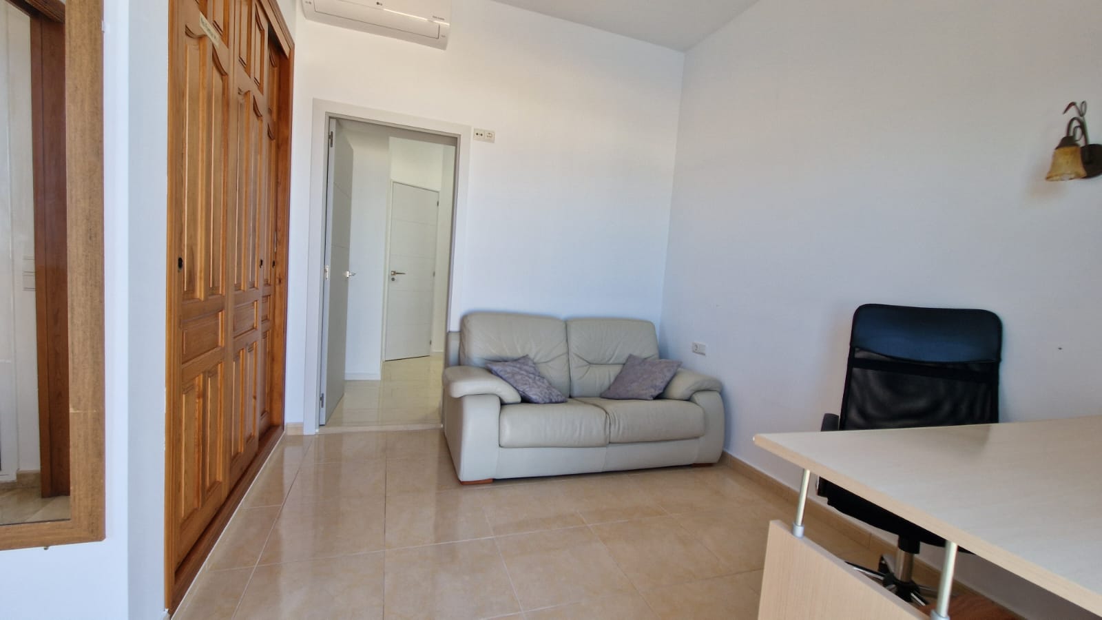 Habitación luminosa con armario de madera, sofá de cuero y escritorio con silla de oficina.
