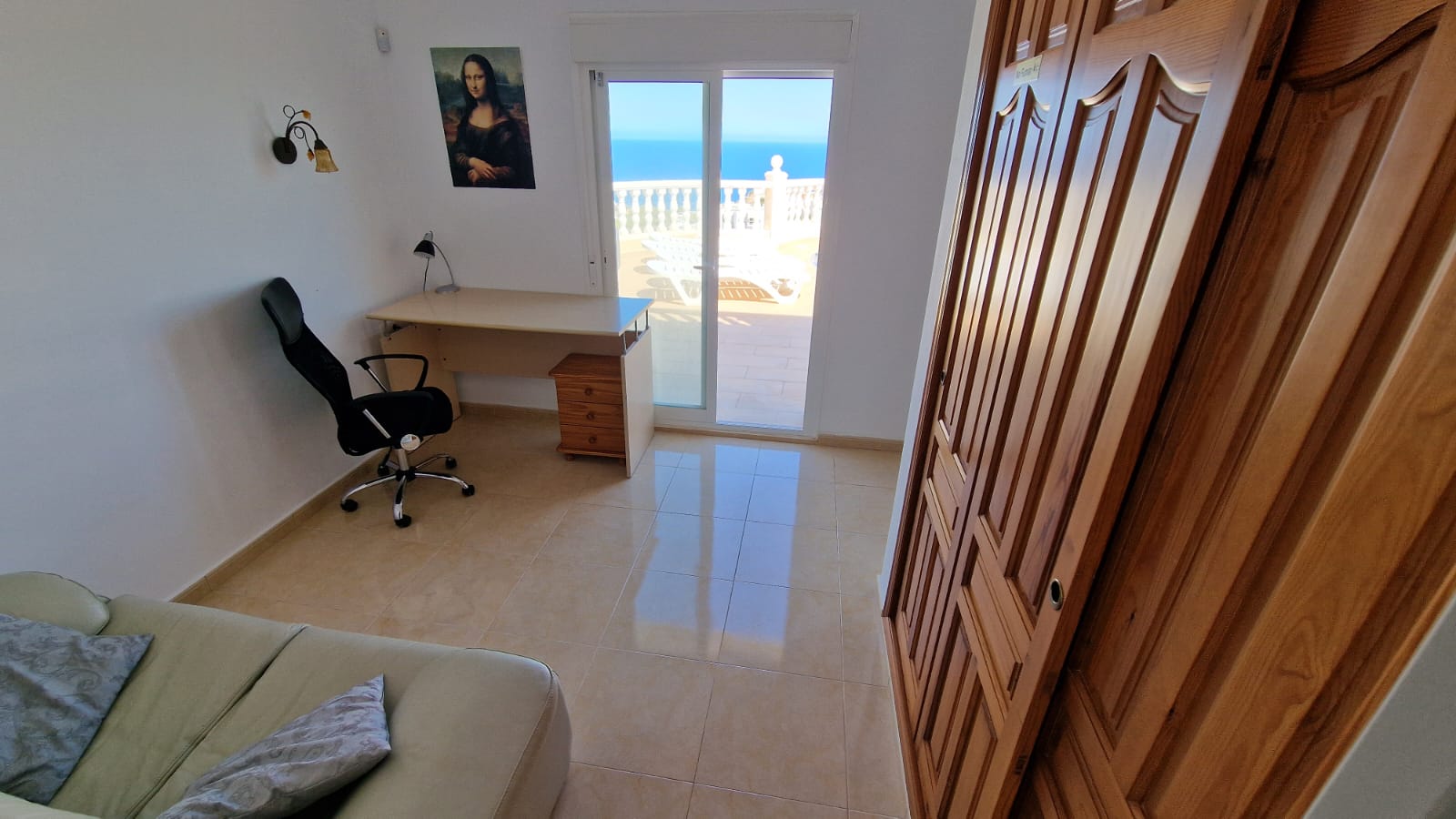 Habitación luminosa con escritorio, armario de madera y acceso a la terraza con vistas al mar.