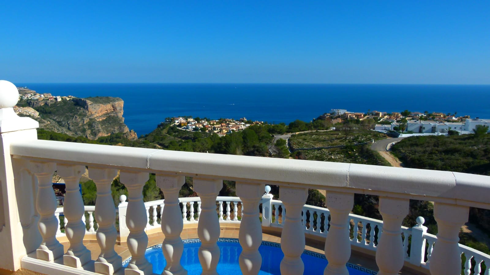 Vista desde la terraza con balaustrada blanca a la piscina y al mar Mediterráneo en Cumbre del Sol.