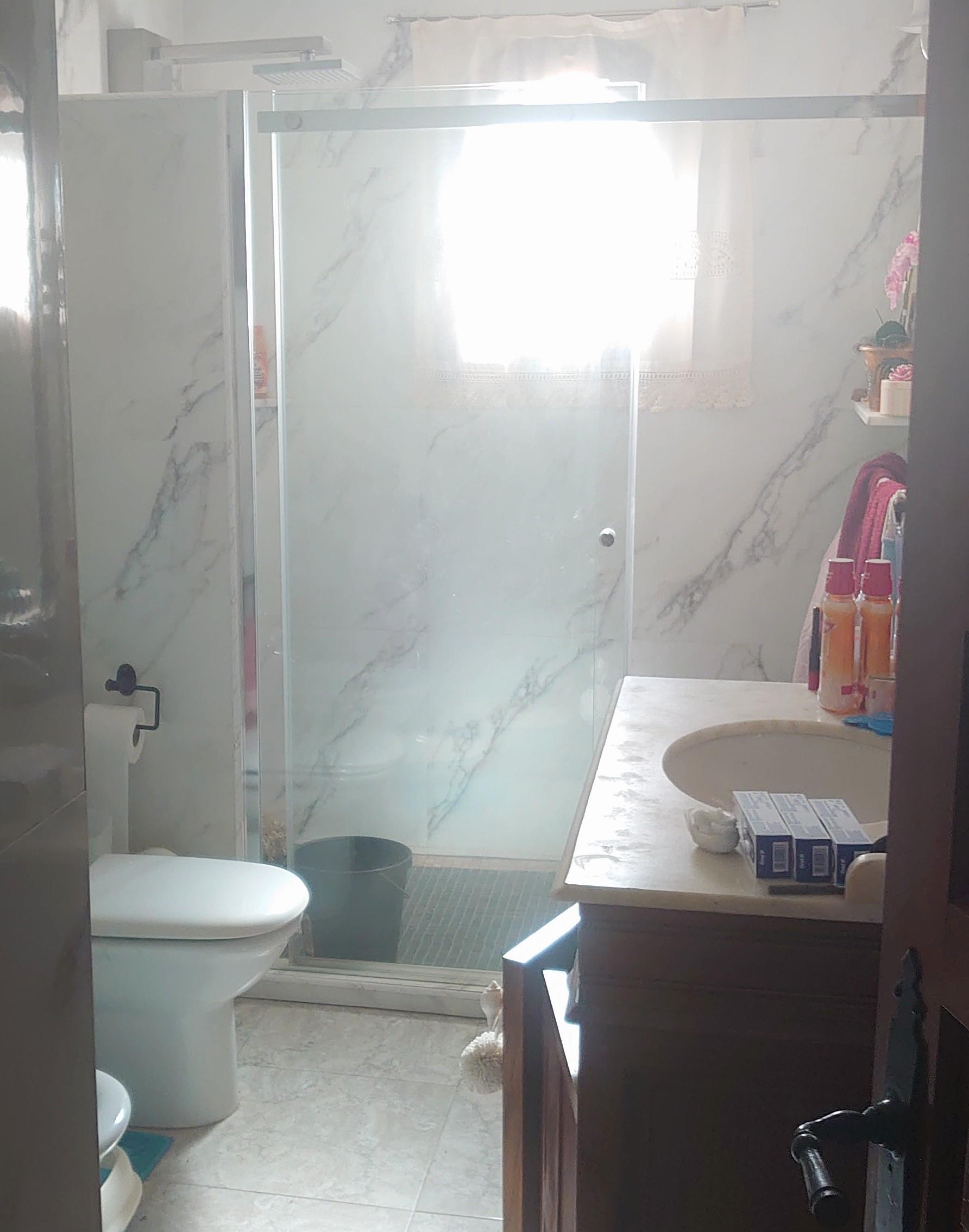 Baño con paredes de azulejos efecto mármol, amplia ducha con mampara de cristal y cabezal de lluvia, y mueble lavabo de madera con encimera de piedra.