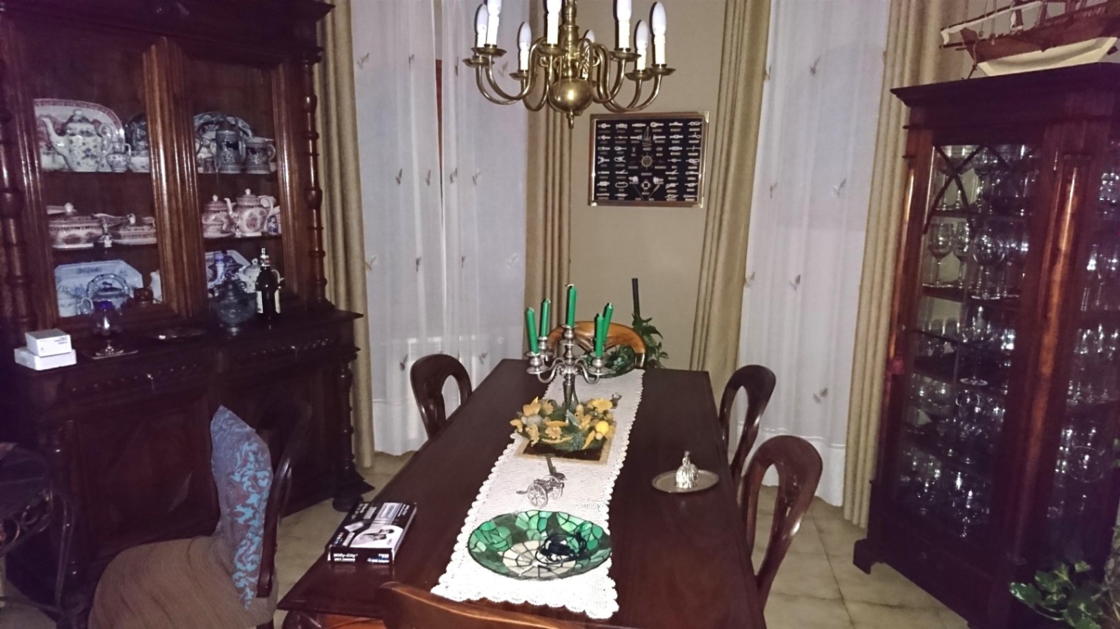 Comedor de estilo clásico con mesa de madera maciza, vitrinas ornamentadas para vajilla y una lámpara de araña de latón sobre un camino de mesa de encaje.