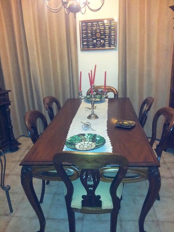 Comedor formal con mesa de madera oscura, sillas de estilo clásico y cortinas de suelo a techo. Incluye detalles decorativos y suelo de baldosa clara.