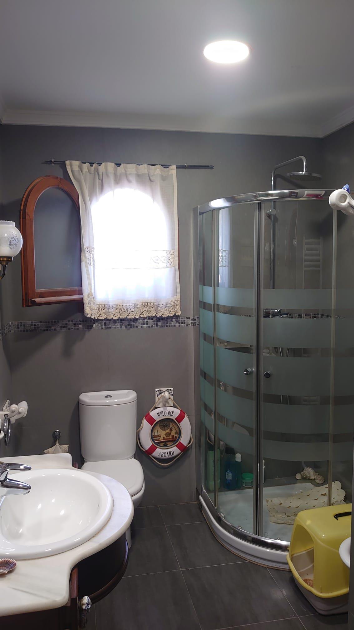 Cuarto de baño con cabina de ducha curva, paredes grises, ventana de arco con marco de madera y detalles de inspiración náutica.