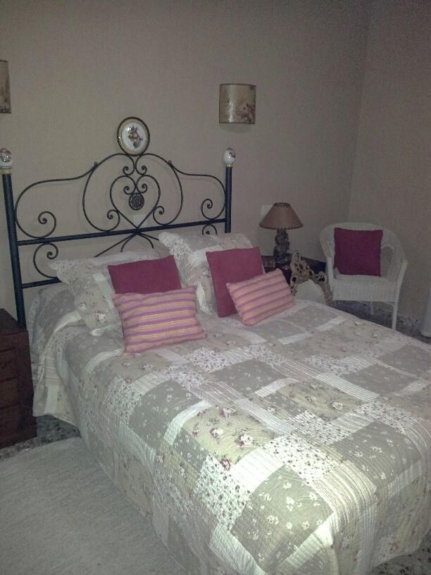 Dormitorio con cabecero de hierro forjado, colcha de patchwork y sillón de mimbre. Incluye iluminación mediante apliques de pared y una lámpara de mesa clásica.