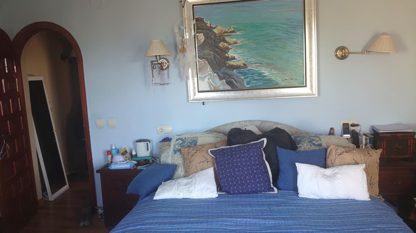 Dormitorio con cama de matrimonio, cabecero decorado con un gran cuadro de temática marina y apliques de pared. Incluye un acceso en arco hacia el vestidor.
