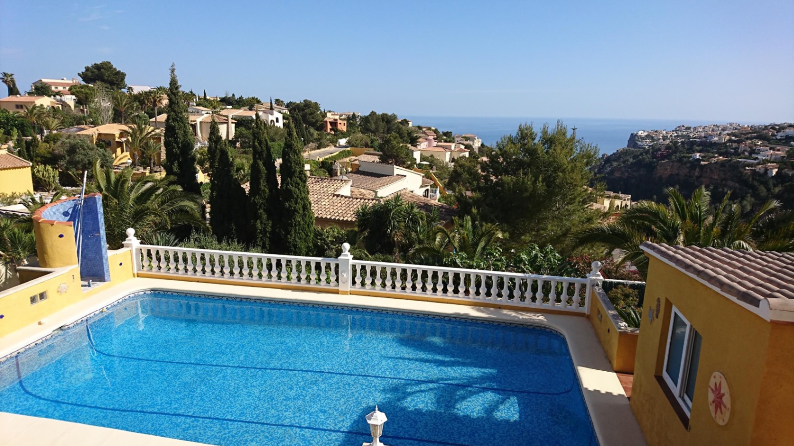 Piscina rectangular con revestimiento de gresite azul, rodeada por una balaustrada blanca y vistas panorámicas al mar Mediterráneo y la costa de Cumbre del Sol.