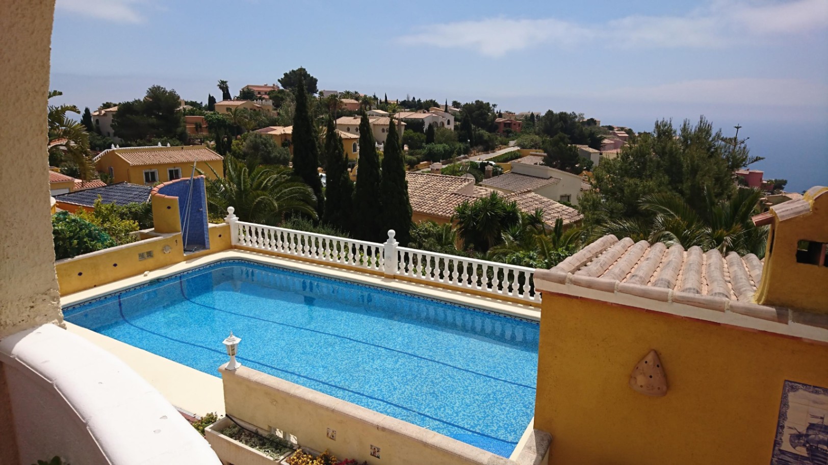 Piscina rectangular de 10x4 con gresite azul, rodeada por una balaustrada blanca y vistas despejadas al entorno residencial y al mar Mediterráneo.