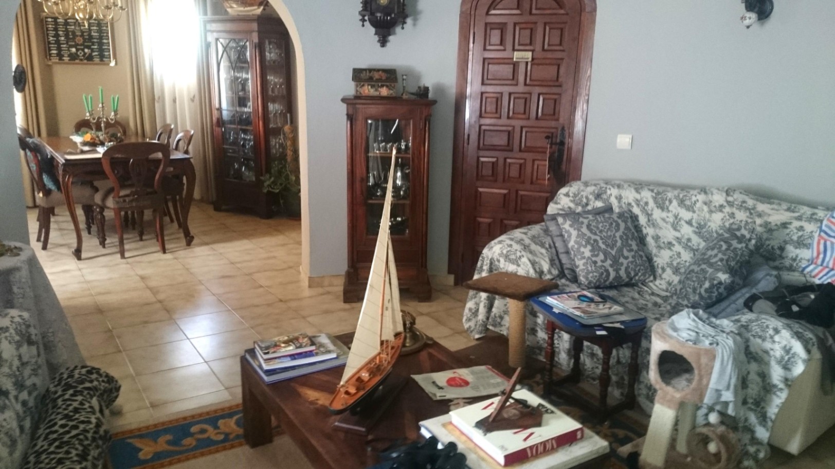 Salón comedor de estilo rústico con suelos cerámicos, muebles de madera oscura, vitrinas clásicas y un arco que conecta con el área de comedor.