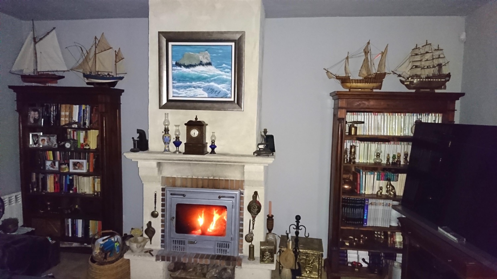 Salón con chimenea de piedra y casete de leña, flanqueada por estanterías de madera clásica con maquetas navales y decoración temática.