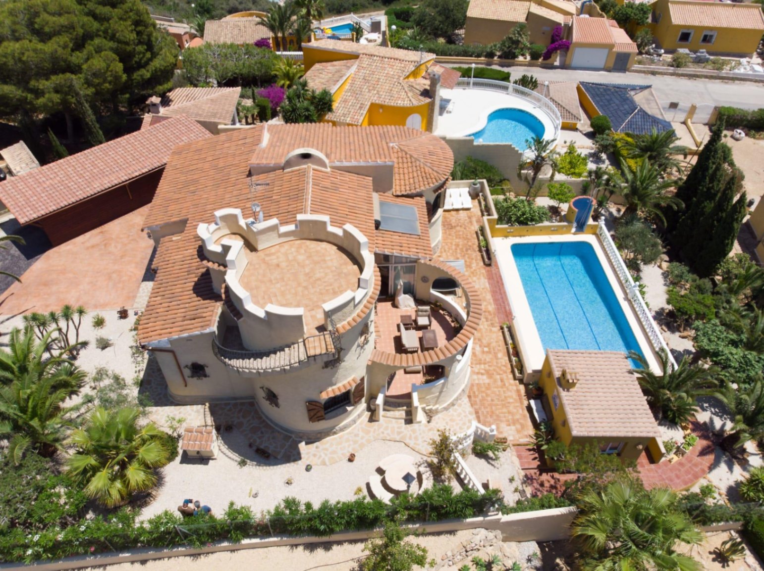 Vista aérea de la villa con su distintiva torre circular, tejados de teja cerámica, piscina de 10x4 metros y zona de cocina exterior en una parcela mediterránea.