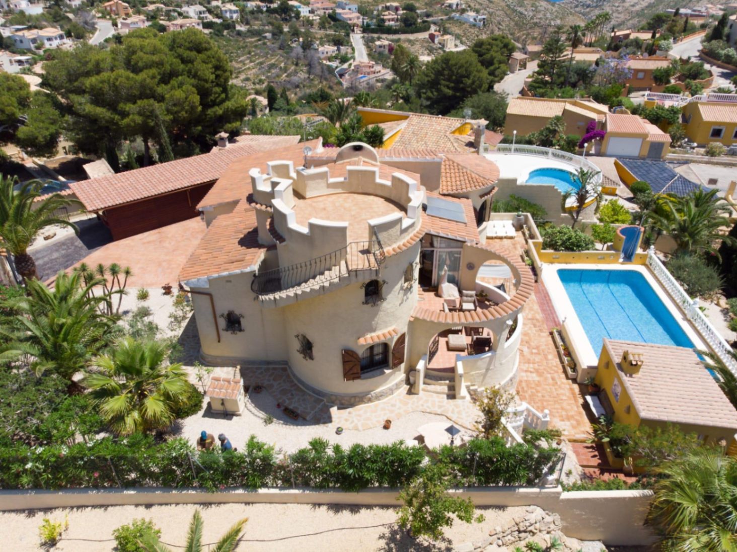 Vista aérea de la villa destacando su torre circular con almenas, la piscina privada y las amplias terrazas de terracota rodeadas de vegetación mediterránea.