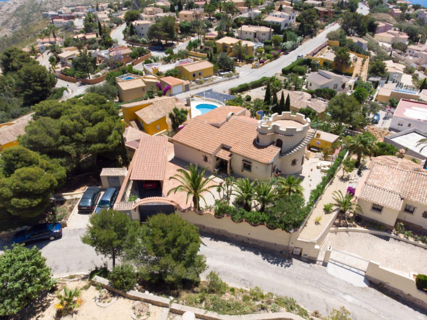 Vista aérea de la villa destacando su torreón almenado, tejado de teja cerámica y jardín mediterráneo con palmeras en una parcela elevada.