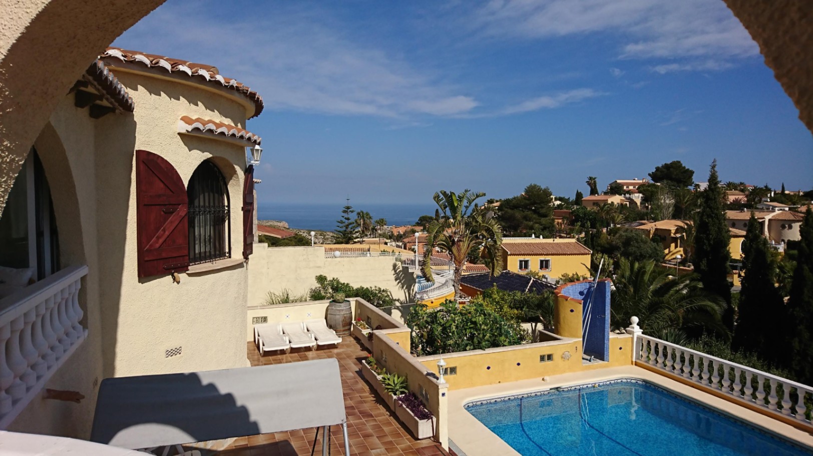 Vista elevada de la zona exterior con piscina rectangular, solárium de terracota y torre con contraventanas de madera, ofreciendo vistas panorámicas al mar Mediterráneo.