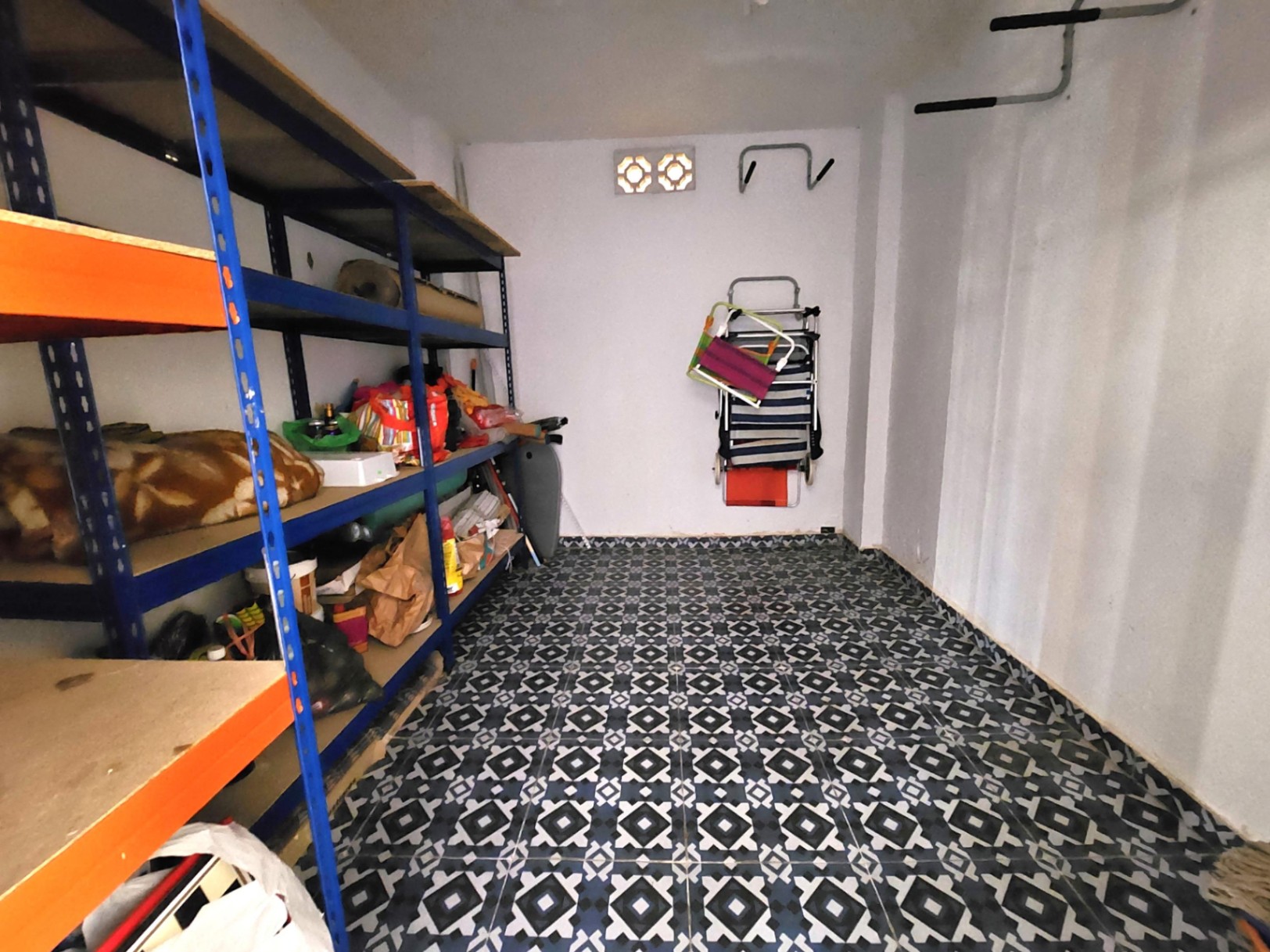 Amplio trastero de 12 m² con suelo de baldosa decorativa, estanterías metálicas de gran capacidad y paredes blancas con ventilación natural.