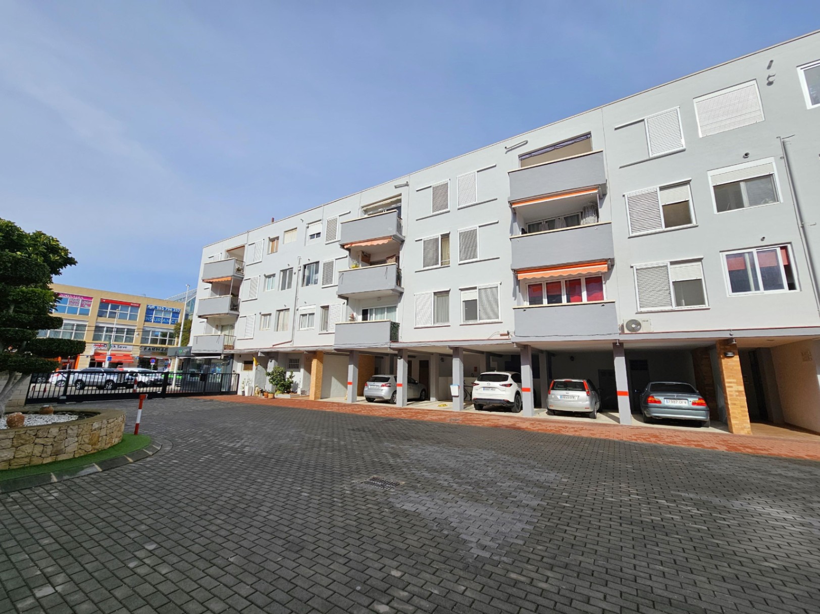 Fachada exterior del edificio en Jávea con zona de aparcamiento privado cubierto y balcones con toldos naranjas.