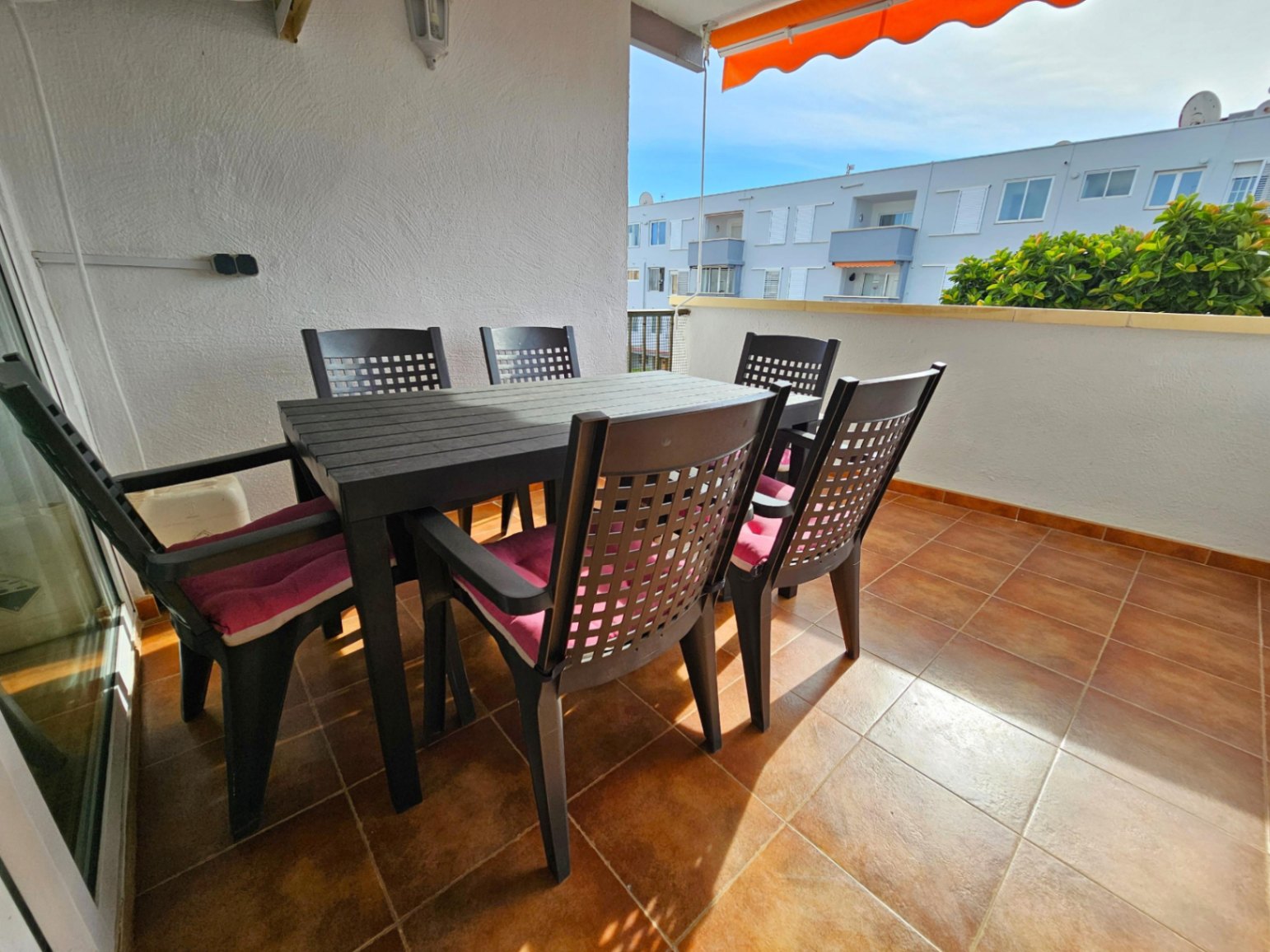 Terraza exterior con suelos de gres cerámico, equipada con un conjunto de comedor para seis personas y un toldo extensible en tonos cálidos.