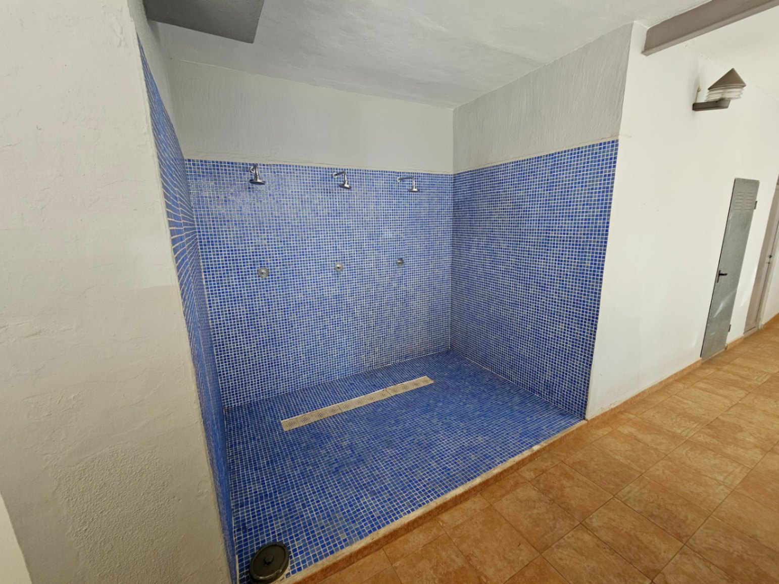 Zona de duchas comunitarias revestida con gresite azul, ideal para eliminar la arena tras un día en la playa. Cuenta con tres tomas de agua y un práctico desagüe lineal.