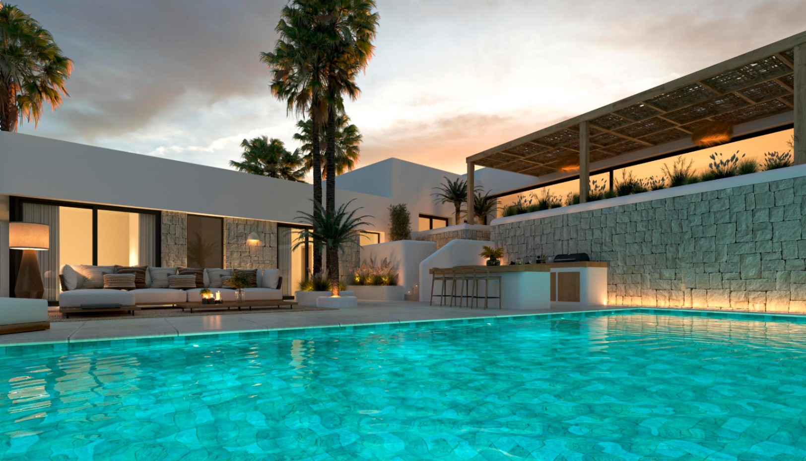 Terraza exterior con piscina iluminada, zona de estar y cocina de verano bajo una pérgola de madera con muros de piedra natural.