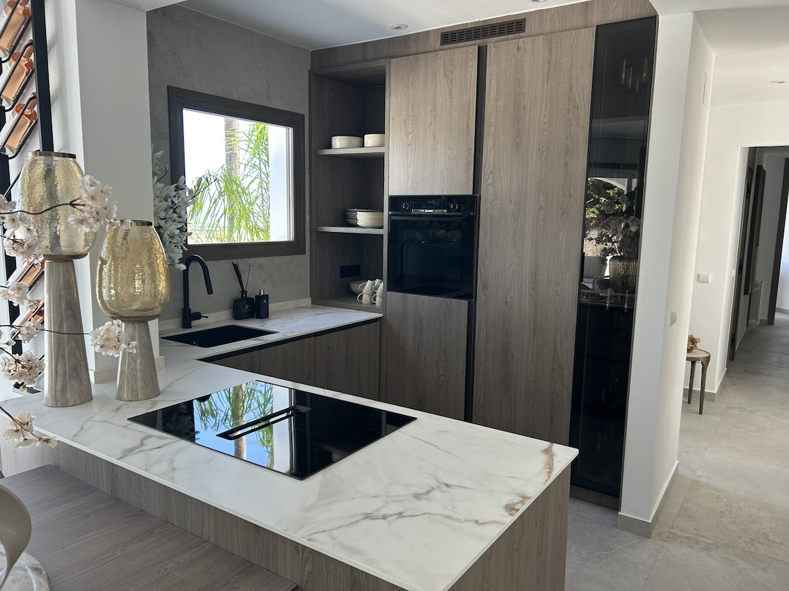 Cocina integrada con armarios de madera, encimera de efecto mármol y placa de inducción con extractor integrado.