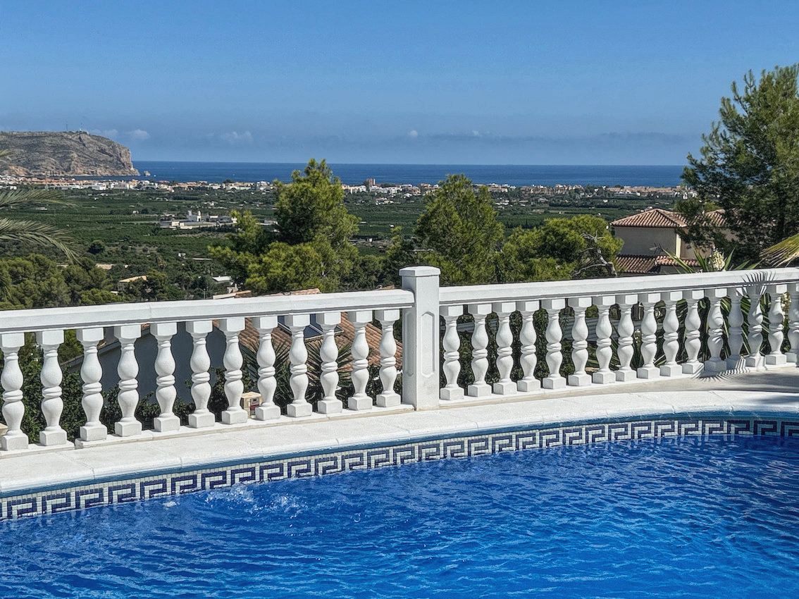 Piscina con borde de mosaico y balaustrada blanca que ofrece vistas panorámicas al mar Mediterráneo, el valle y los acantilados costeros.