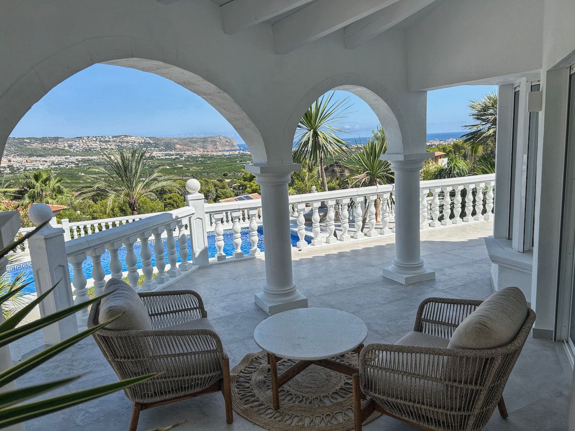 Terraza cubierta con arcos blancos, mobiliario de mimbre y vistas panorámicas al valle, el mar y la piscina privada de la villa.