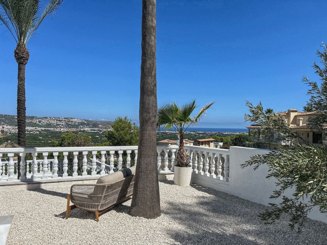 Terraza exterior con suelo de grava blanca, mobiliario de diseño y balaustrada clásica que ofrece vistas panorámicas al valle y al mar Mediterráneo.