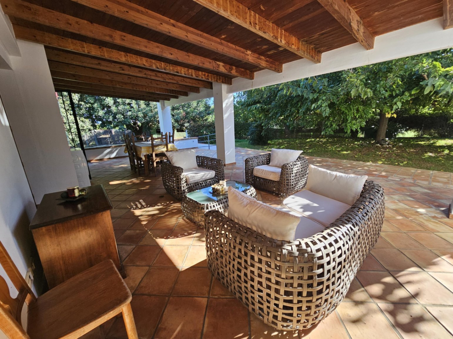 Amplia naya cubierta con techos de vigas de madera y suelos de barro artesanal, equipada con mobiliario de mimbre y vistas directas al jardín.