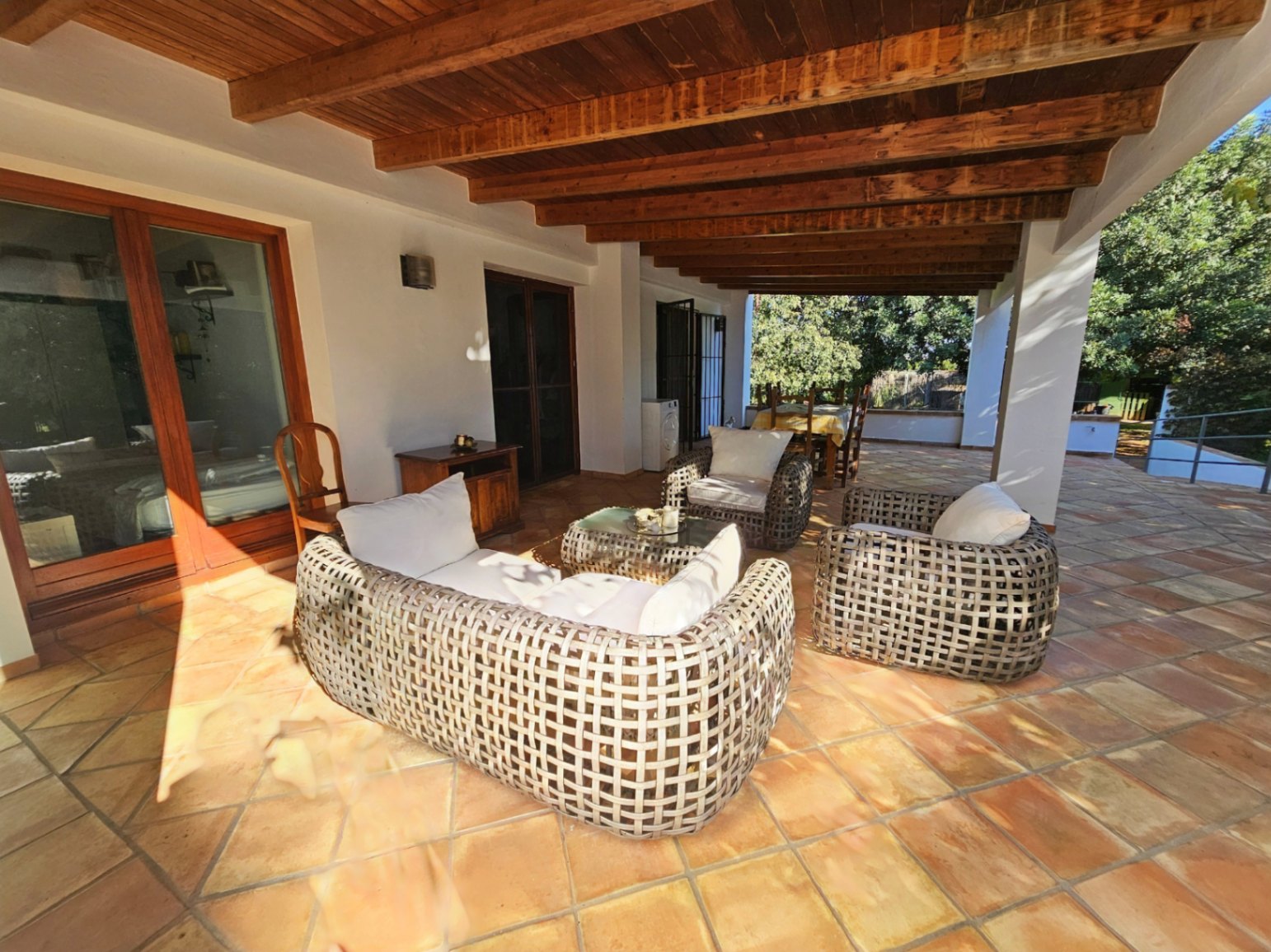 Amplia naya cubierta con vigas de madera vista y suelos de barro manual. Dispone de una zona de estar con muebles de mimbre y acceso directo a las estancias interiores.