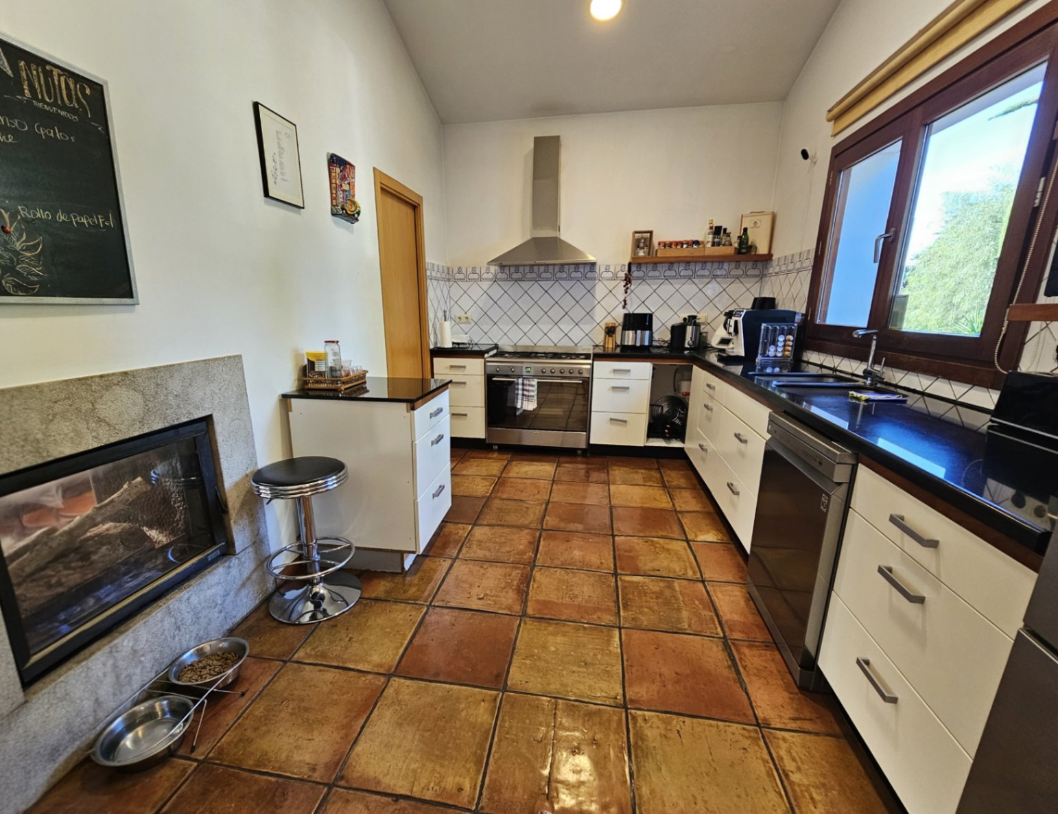 Cocina rústica con suelos de barro hechos a mano, encimeras oscuras y una chimenea de doble cara integrada en un marco de piedra natural.