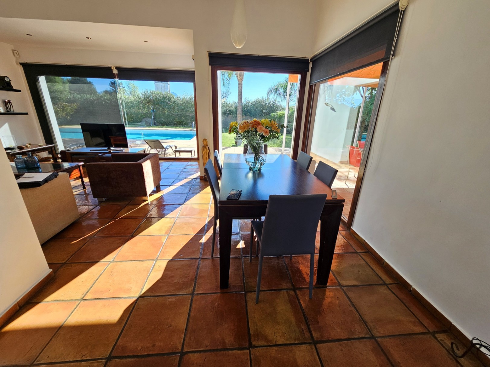 Comedor con suelos de barro hechos a mano y grandes ventanales que ofrecen vistas directas a la piscina y al jardín mediterráneo.