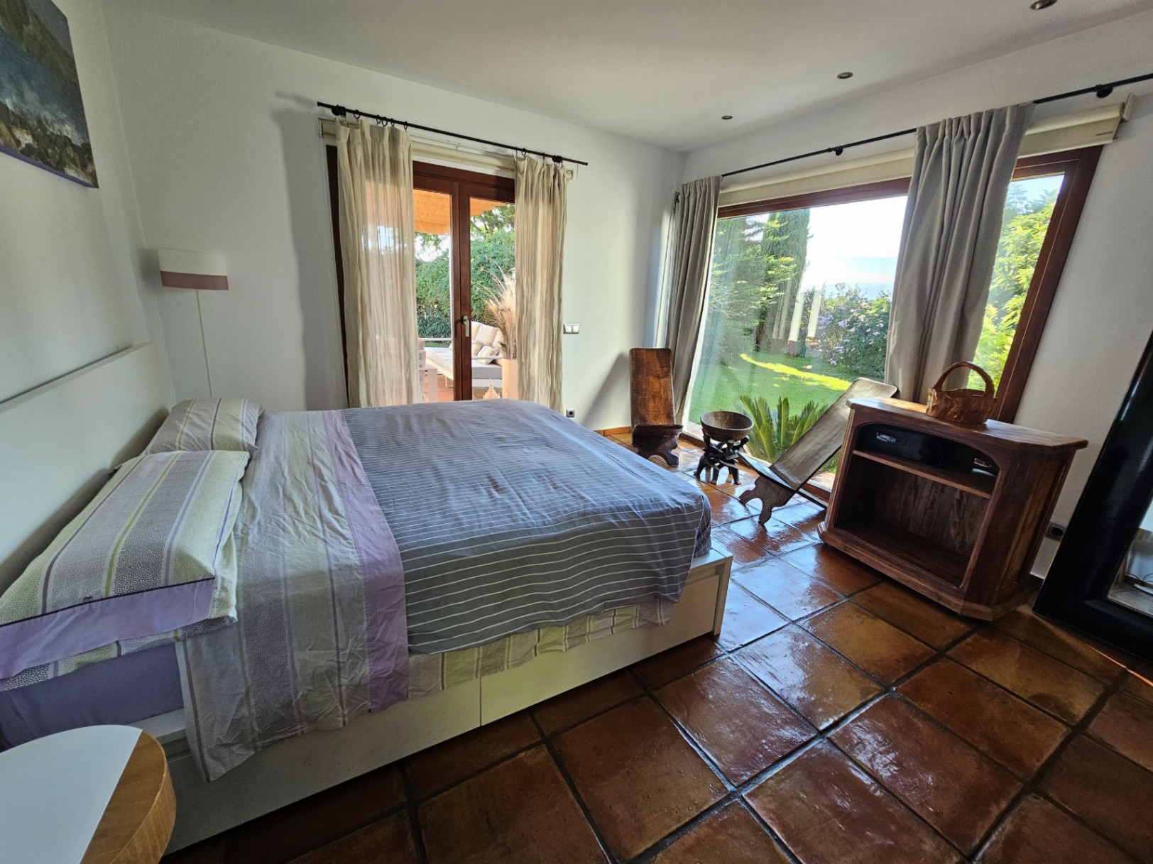 Dormitorio luminoso con suelos de barro hechos a mano, acceso directo al jardín y grandes ventanales que ofrecen vistas despejadas a la zona verde privada.