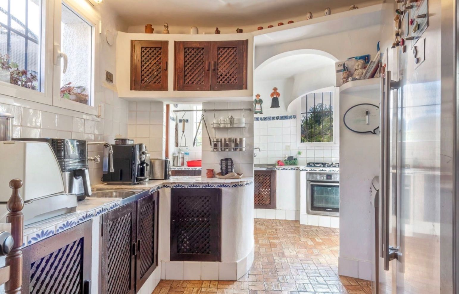 Cocina de estilo rústico con armarios de madera oscura y celosía, encimeras con azulejos blancos y detalles azules, y suelos de terracota tradicional.
