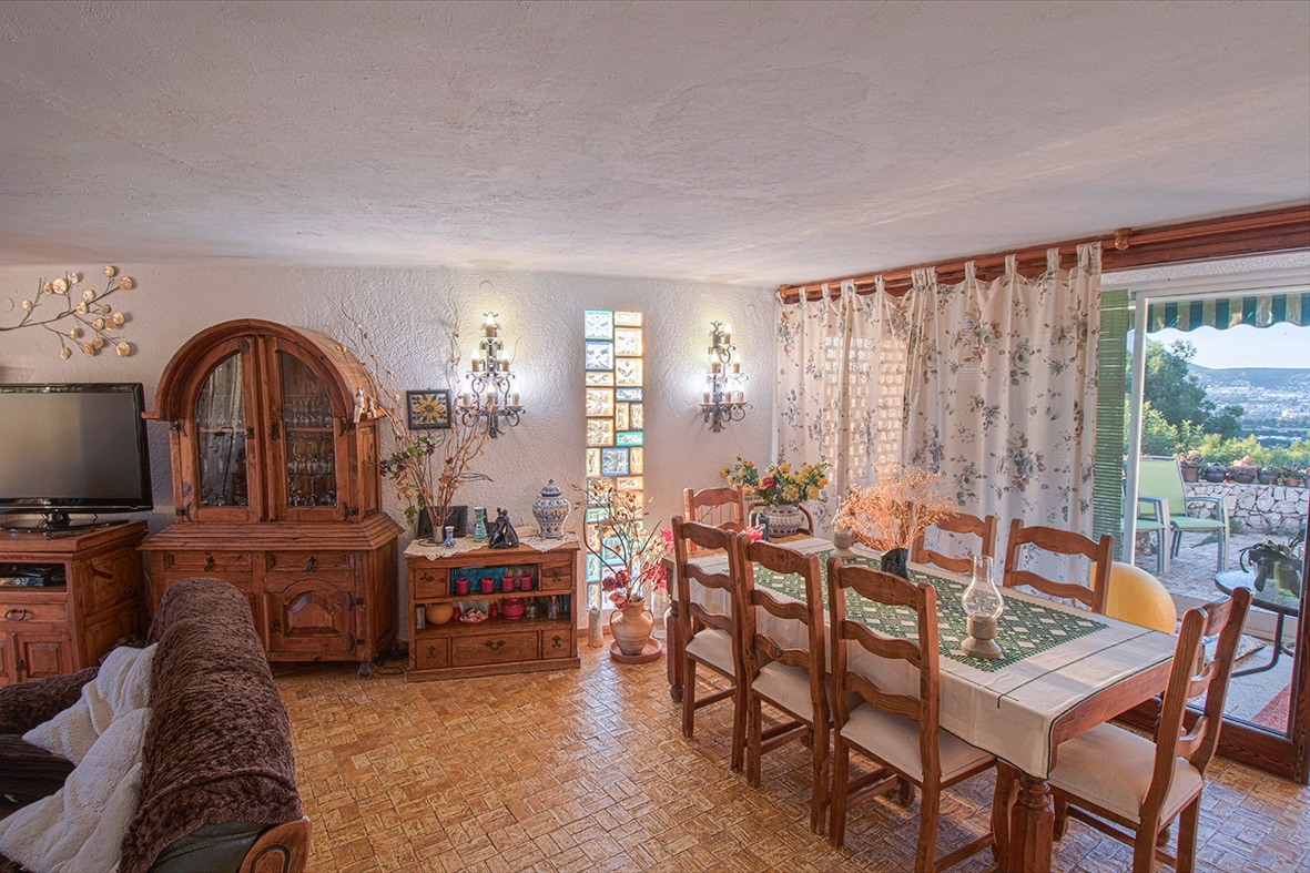 Comedor rústico con mobiliario de madera tradicional, suelos cerámicos y acceso directo a la terraza mediante grandes ventanales con vistas al valle.