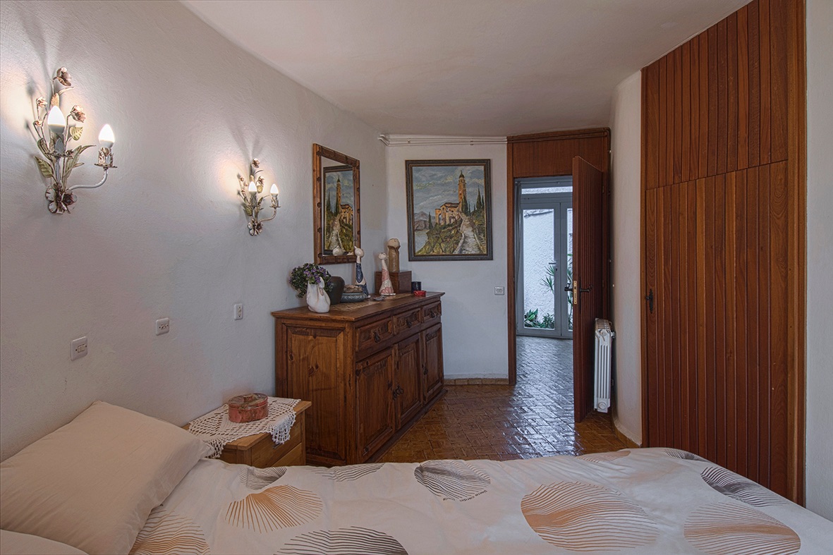 Dormitorio con armario empotrado de madera, aparador rústico y apliques decorativos. El suelo cerámico y la calefacción por radiador aportan confort al espacio.