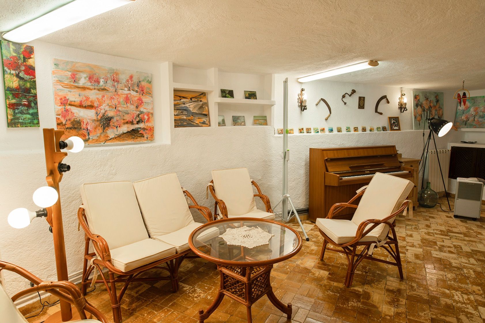 Sala de estar con mobiliario de bambú, suelos de terracota y paredes blancas texturizadas. Incluye un piano de pared, nichos con obras de arte y una mesa de centro de cristal.