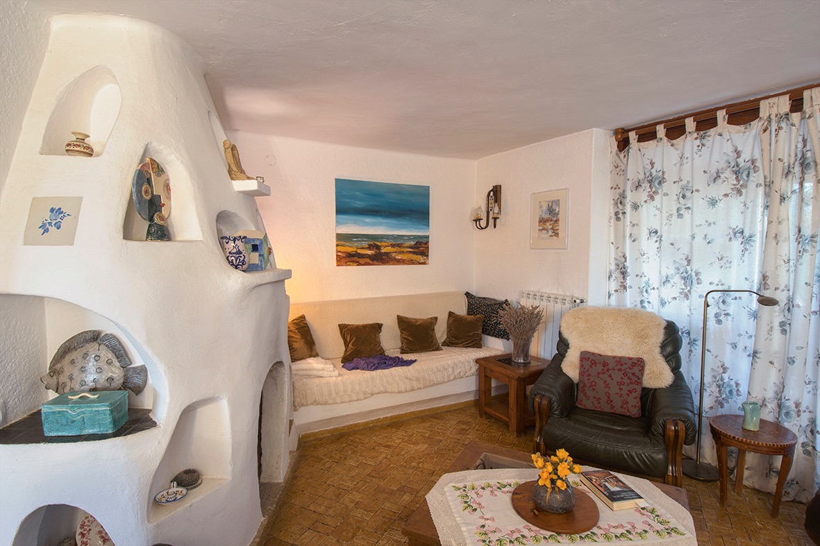 Salón acogedor con una chimenea escultórica de obra blanca con hornacinas decorativas, suelos de gres rústico y mobiliario de estilo tradicional.
